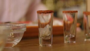 A Shot Glass with A Spiced Rim Holds an Oyster and Cocktail Sauce, with More Shooters Lined up In the Background