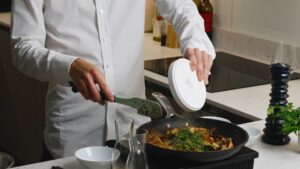 A Person Sprinkles Fresh Parsley from A White Bowl Into a Skillet of Sautéed King Oyster Mushrooms