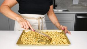 A Person Spreads Seasoned Oyster Crackers Evenly on A Baking Sheet Using a Spatula